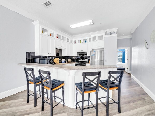 A modern kitchen with white cabinets, a central island with bar stools, and a stainless steel refrigerator.