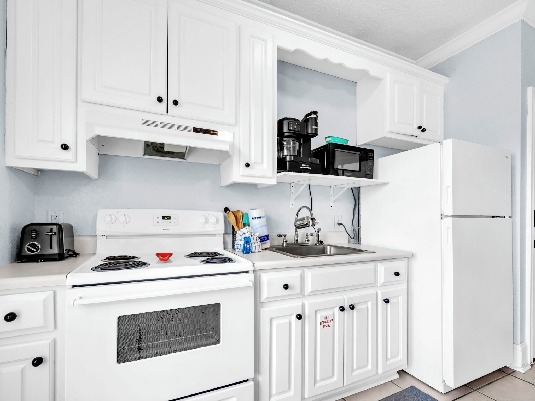 Une cuisine avec des meubles blancs, une cuisinière, un évier et un réfrigérateur.