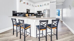 Uma cozinha moderna com armários brancos, uma ilha central com banquetas e uma geladeira de aço inoxidável.