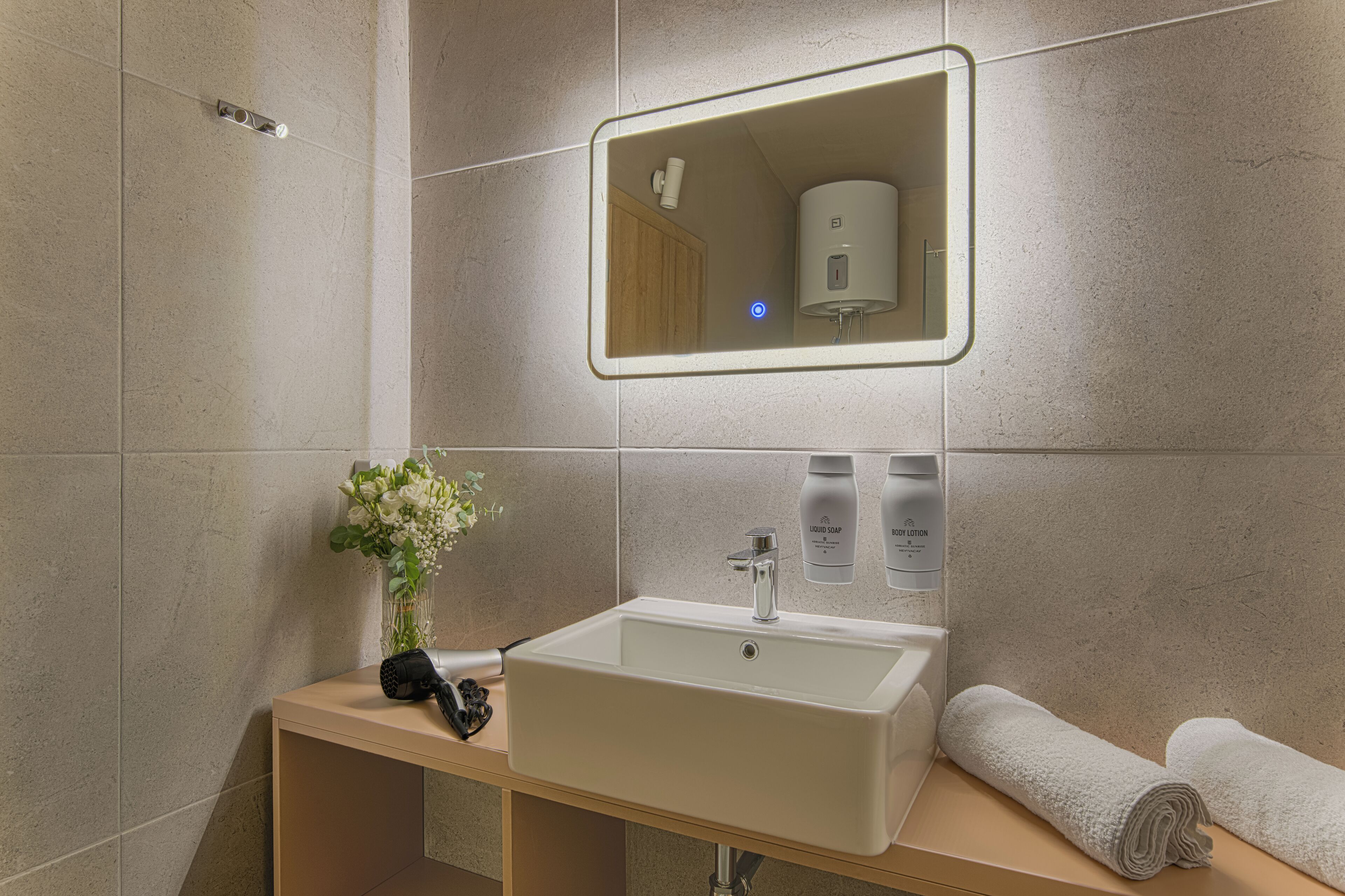 A modern bathroom with a rectangular sink, a mirror, a towel, and a vase with flowers.