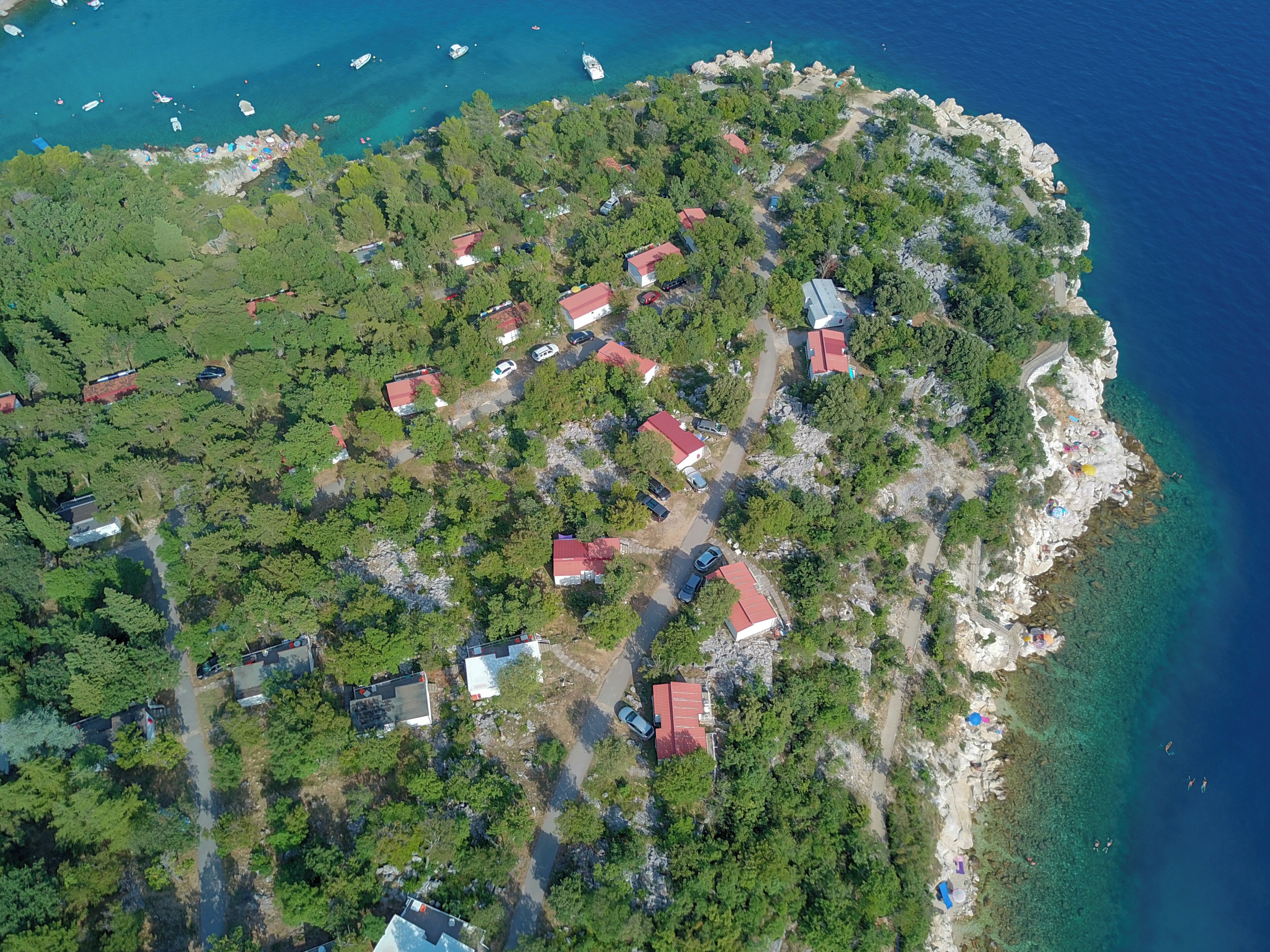 An aerial view of a coastal village with houses, clear blue waters, and rocky terrain.