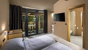 Hotelkamer met twee bedden, een bureau, een televisie en een glazen schuifdeur naar een buitenruimte met een tafel en stoelen.