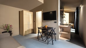 Een compacte keuken met een eethoek, een televisie bevestigd boven het aanrecht, en een klein zithoekje met een tafel en stoelen.