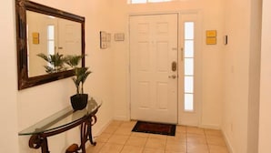 A hallway with a white door, a glass console table with a potted plant, a large mirror, and a window above the door. - Cozy 4 Bedroom Villa with 3 Bathrooms and South Facing Pool (CLERMONT)