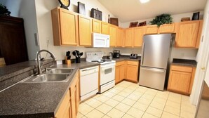 A kitchen with wooden cabinets, a stainless steel refrigerator, a white stove, and a granite countertop. - Cozy 4 Bedroom Villa with 3 Bathrooms and South Facing Pool (CLERMONT)