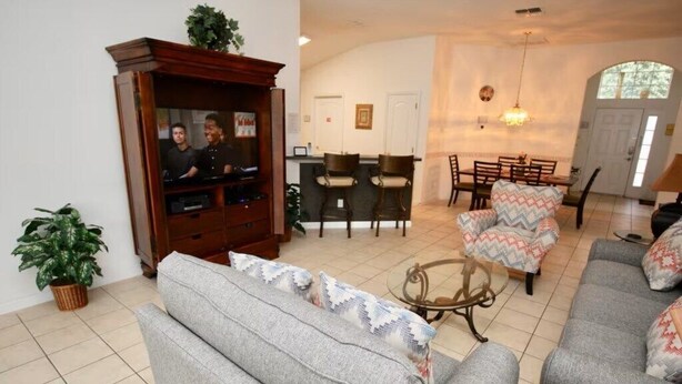 A living room with a sofa, a television, a dining area with chairs, and a small table. - Cozy 4 Bedroom Villa with 3 Bathrooms and South Facing Pool (CLERMONT)