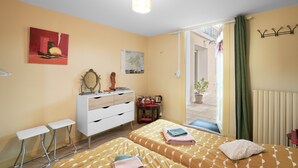 A room with two beds, a white dresser, a small table, a map on the wall, and a view of the outside.