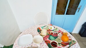 A dining table with a colorful tablecloth, a white chair, a plate with food, a glass, and a spoon.