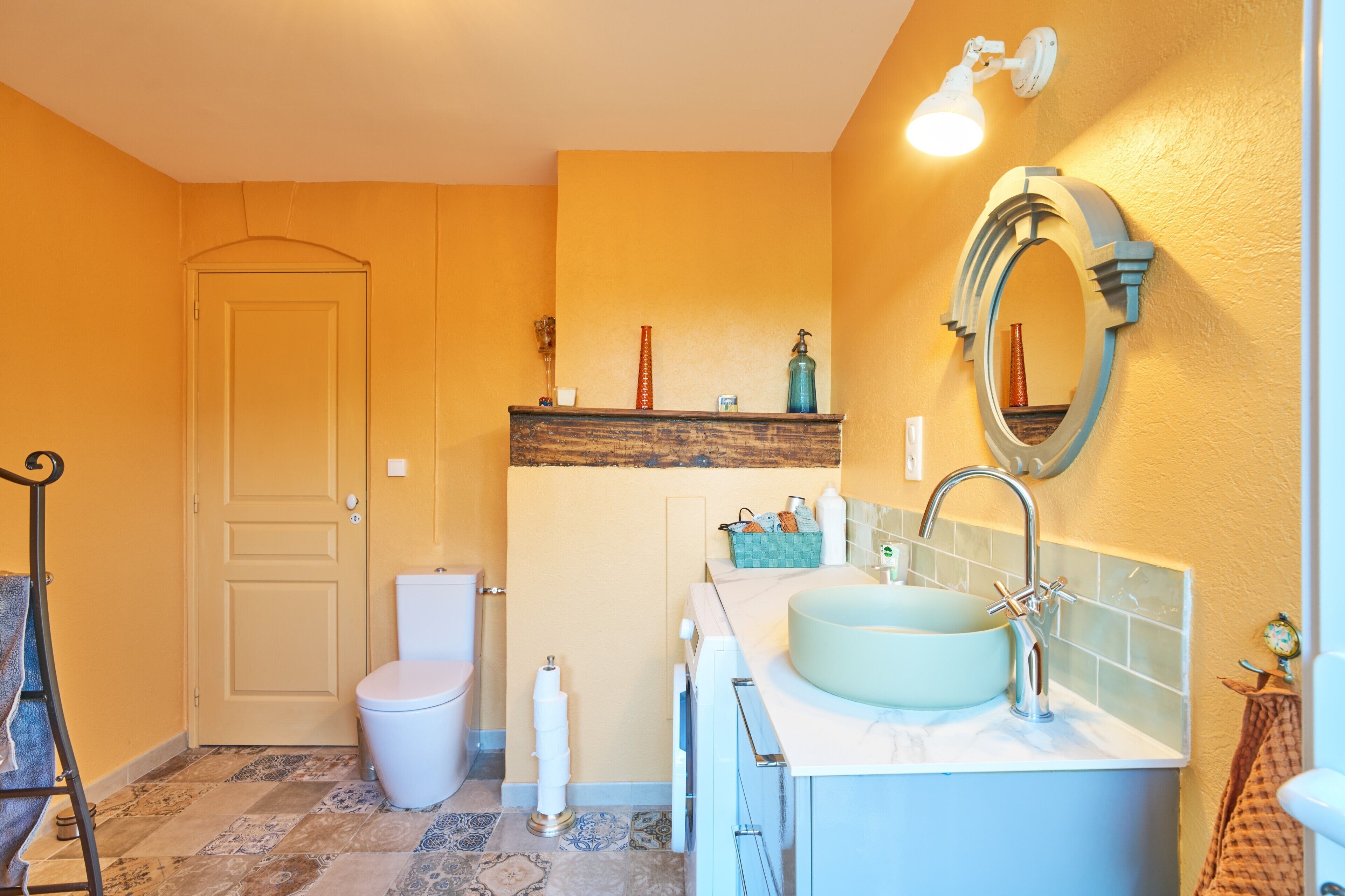 Une salle de bain équipée de toilettes, d’un lavabo, d’un miroir et d’une étagère contenant des articles de toilette.