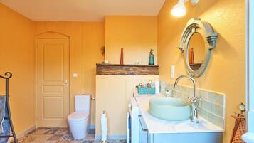 Une salle de bain équipée de toilettes, d’un lavabo, d’un miroir et d’une étagère contenant des articles de toilette.