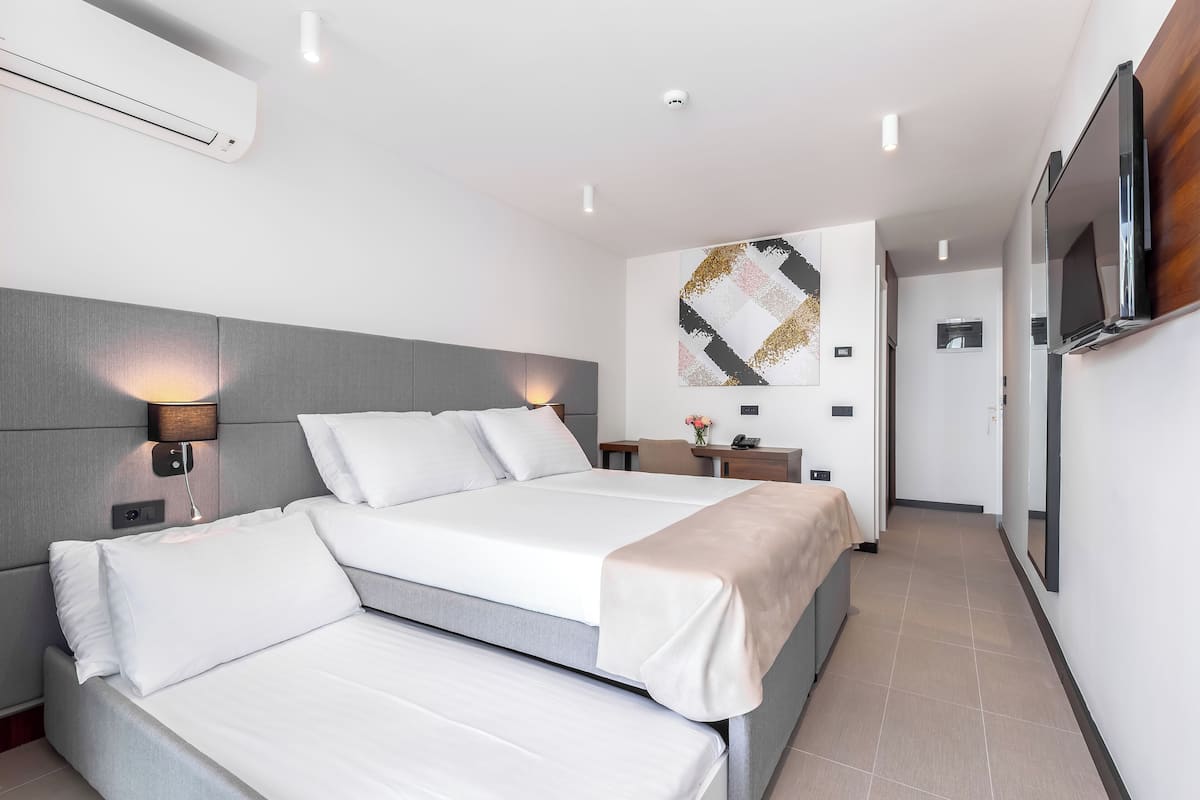 Una habitación de hotel moderna con dos camas, un televisor montado y una obra de arte en la pared.
