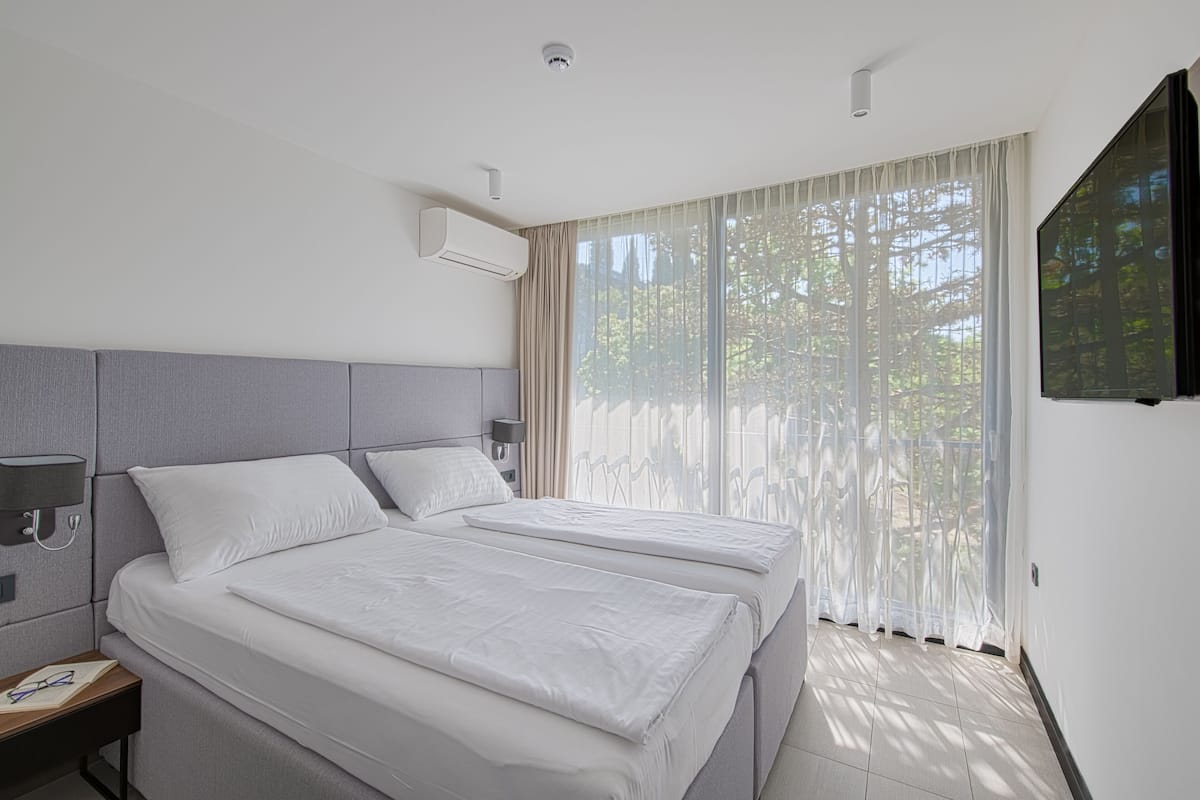 Una habitación de hotel moderna con dos camas, un televisor de pantalla plana y un ventanal con cortinas translúcidas.