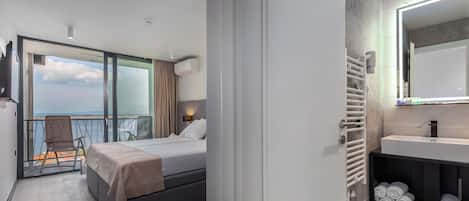 Ett modernt hotellrum med en balkong, en säng, ett badrum med en spegel och en hylla med handdukar.