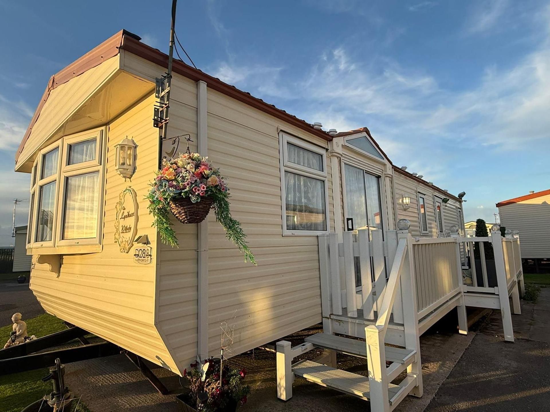 A mobile home with a porch, a hanging flower basket, and a visible mailbox.
