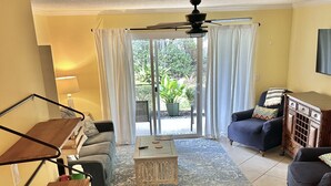 A living room with a wooden coffee table, a sofa, a chair, and a dining area with a wooden table and chairs. - T13 Ocean Walk downstairs king bed pool pickleball (St. Simons Island)