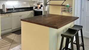 A kitchen with white cabinets, a wooden island, and a black stool. - T13 Ocean Walk downstairs king bed pool pickleball (St. Simons Island)
