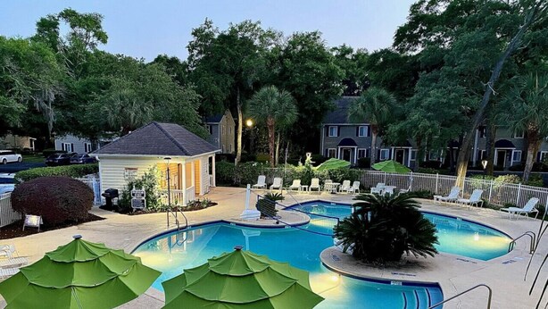 A swimming pool area with multiple pools, lounge chairs, and umbrellas. - T13 Ocean Walk downstairs king bed pool pickleball (St. Simons Island)