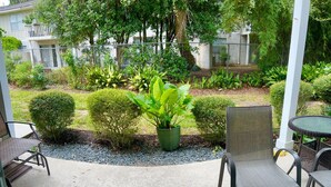 An outdoor patio area with concrete flooring, surrounded by greenery and a fence. - T13 Ocean Walk downstairs king bed pool pickleball (St. Simons Island)