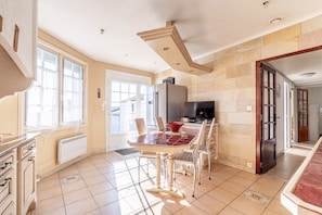 Uma cozinha com uma mesa de jantar, cadeiras, geladeira e televisão.