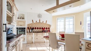 A kitchen with a stove, oven, and cabinets, a dining table with chairs, and a window with blinds.