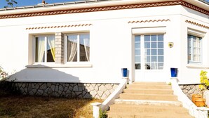 A white building with a stone base, a set of steps leading to the entrance, and a flag on the door.