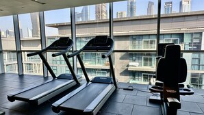 A gym with treadmills and a weight machine, large windows with a city view. - City Walk 1BR Near Burj Khalifa Dubai Mall (Dubai)
