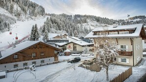 Ein verschneites Dorf mit Holzhäusern, einer Seilbahn und einem Berg im Hintergrund.