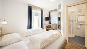 Ein Hotelzimmer mit zwei Betten, einem Schreibtisch, einem Stuhl, einem Fernseher und einer Dusche.