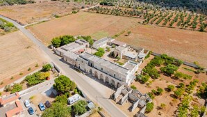 An aerial view of a historic building with a central courtyard, surrounded by agricultural fields and sparse vegetation.