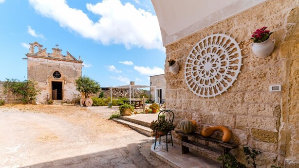 A courtyard with a stone wall, a decorative metal piece, and potted plants.