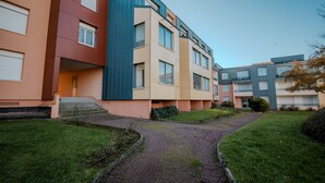 A modern multi-story residential building with a central courtyard, a gravel pathway, and a small grassy area.