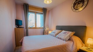 A bedroom with a bed, a bedside table with a lamp, a clock on the wall, and a window with curtains.