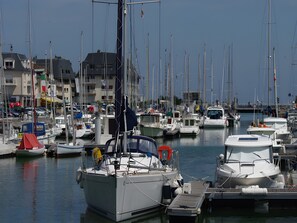 Un puerto deportivo con varias embarcaciones amarradas, edificios al fondo y cielo despejado.