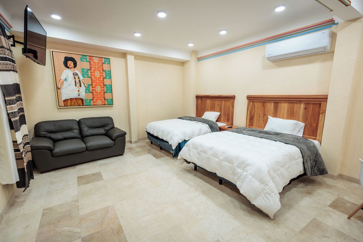 A hotel room with two beds, a sofa, a TV, and an air conditioner.