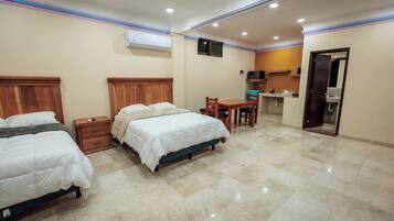 A hotel room with two beds, a small desk, and a kitchenette.