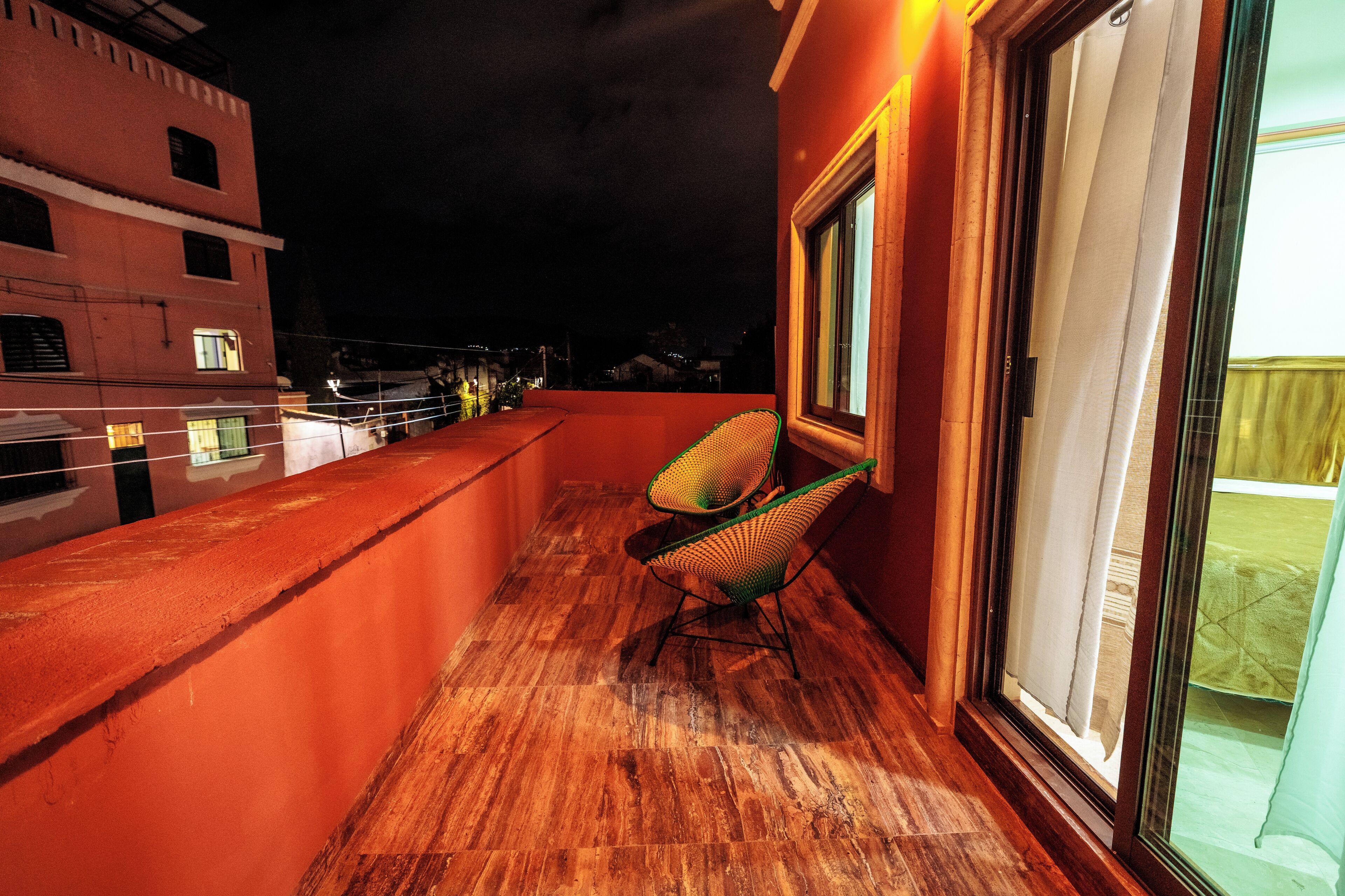 A balcony with a wooden floor, a chair, and a window with curtains.