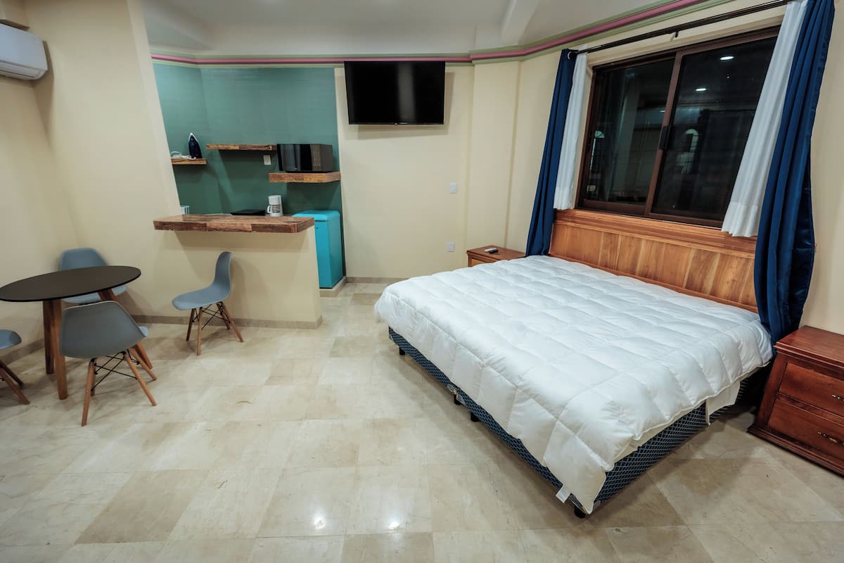 Habitación de hotel con cama, escritorio, silla, televisor y ventana con cortinas.