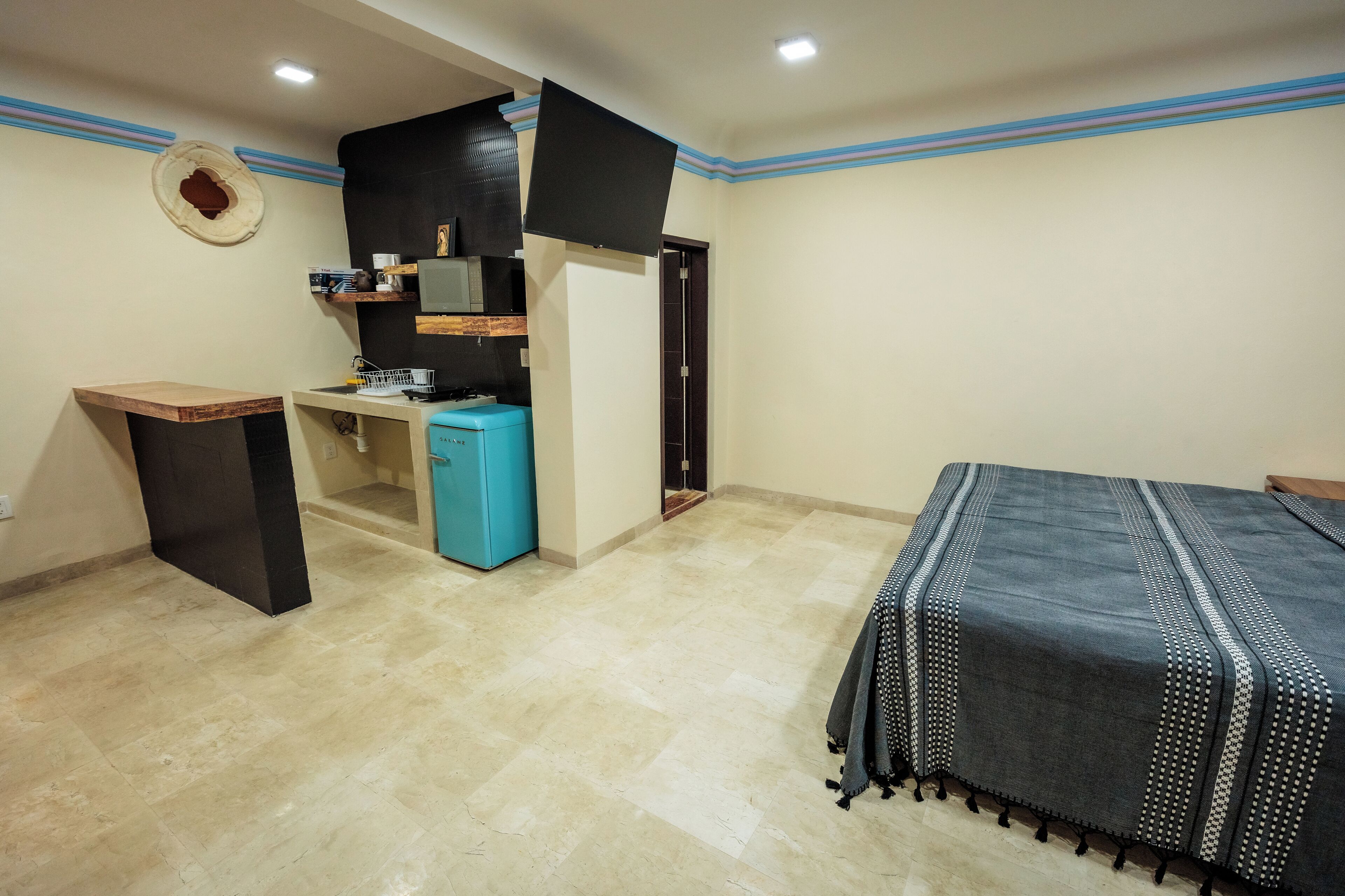 A bedroom with a bed, a desk, a small kitchenette, and a wardrobe.