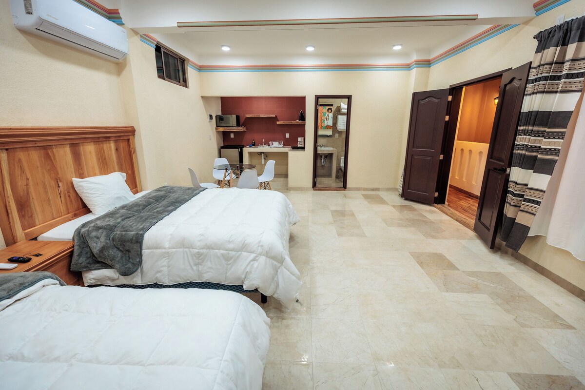 A hotel room with two beds, a small kitchenette, and a bathroom visible through an open door.