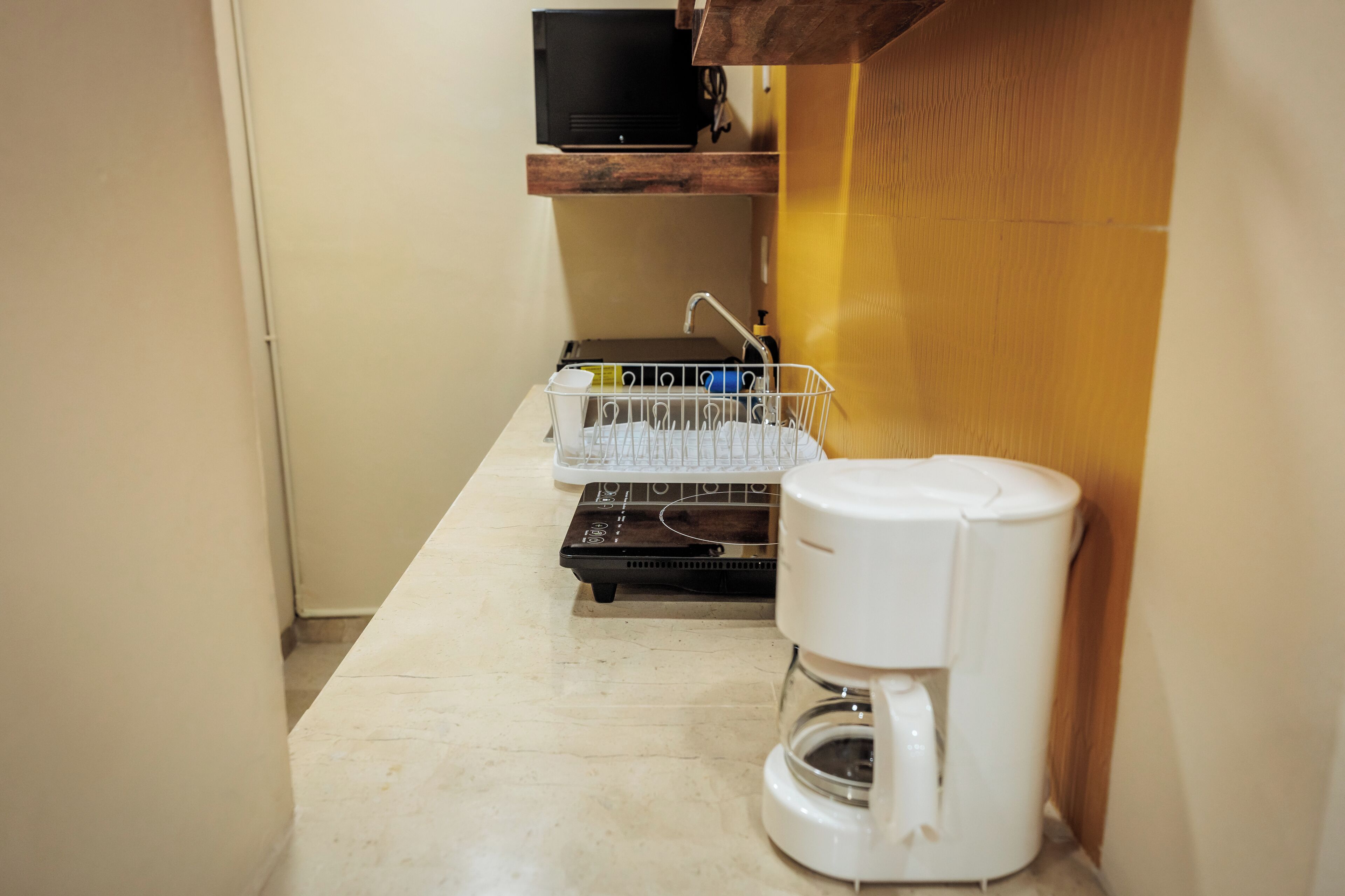 A compact kitchen with a coffee maker, a dish rack, and a microwave.