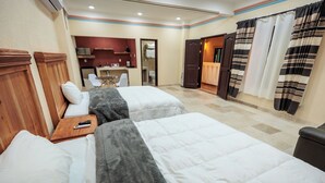 Habitación de hotel con dos camas, un escritorio pequeño, una silla, un espejo y un baño visible a través de una puerta abierta.