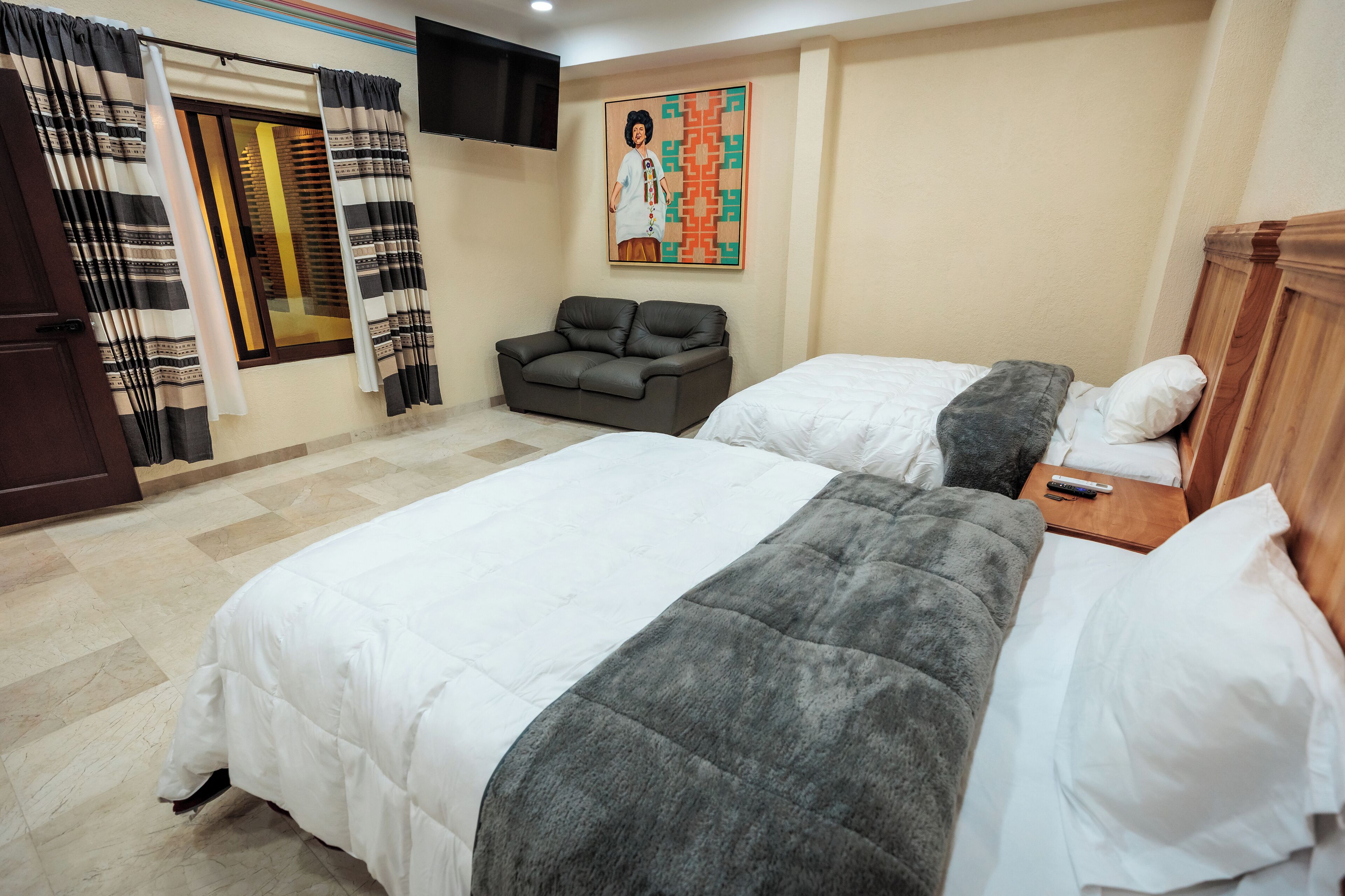 A hotel room with two beds, a sofa, a TV mounted on the wall, and a painting above the sofa.
