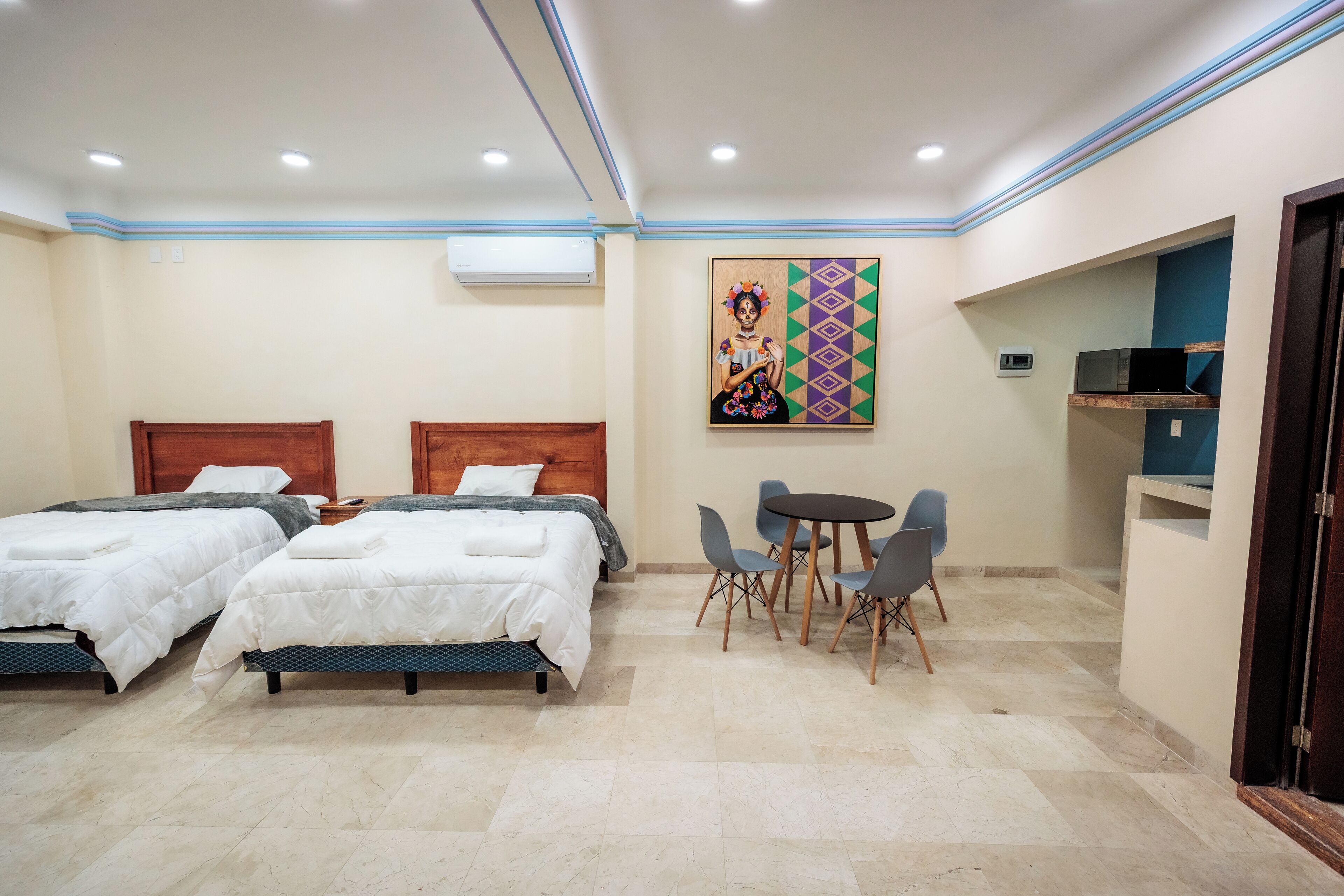 Une chambre d’hôtel avec deux lits, une petite table à manger avec des chaises, un four à micro-ondes et un tableau au mur.