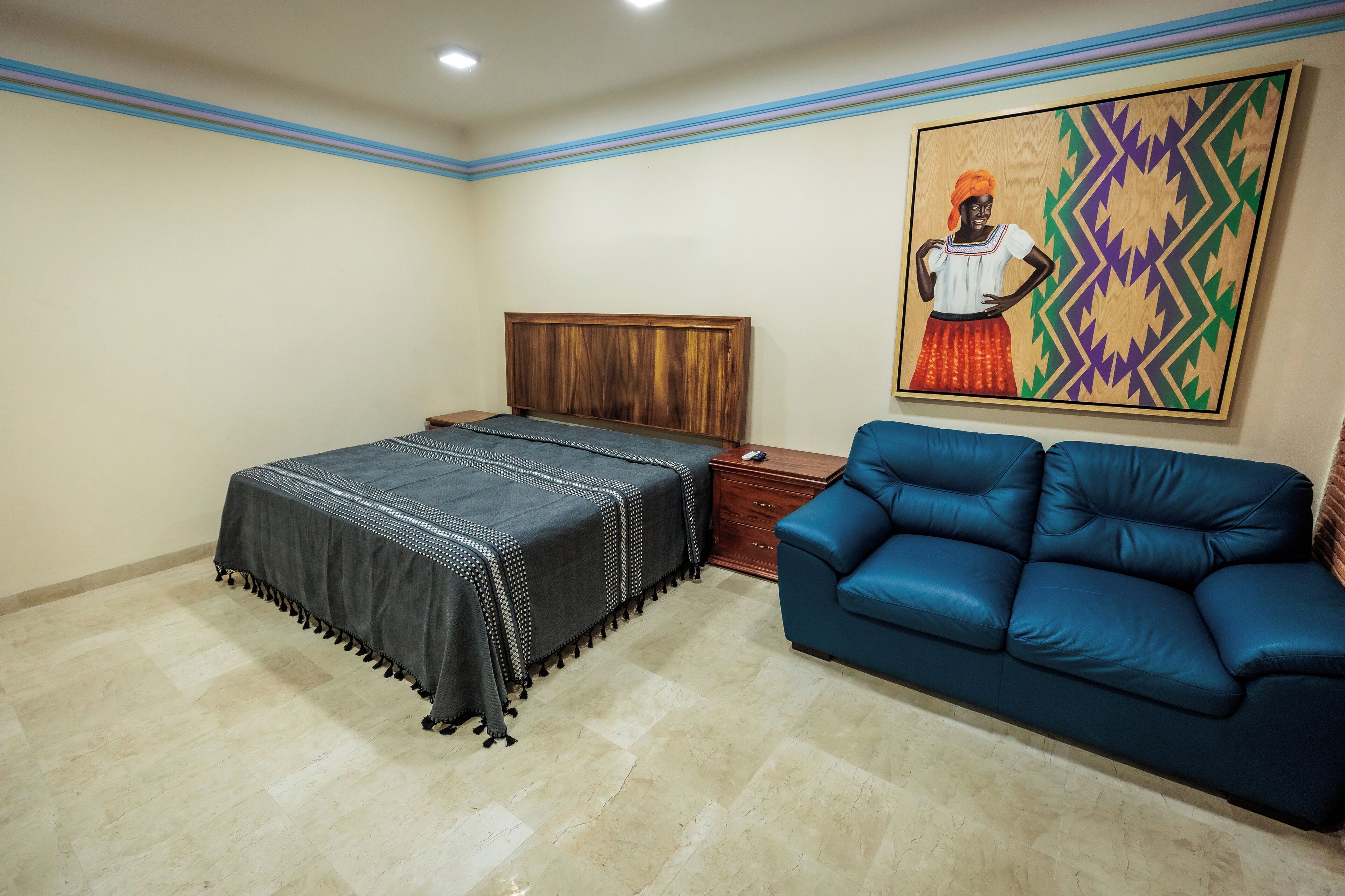 A bedroom with a bed, a blue sofa, a wooden nightstand, and a painting on the wall.