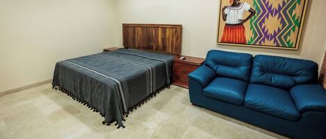 A bedroom with a bed, a blue sofa, a wooden nightstand, and a painting on the wall.