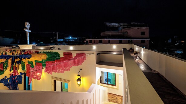 Eine Dachterrasse mit bunten Dekorationen, einem Laternenlicht und Blick auf die nächtliche Skyline.