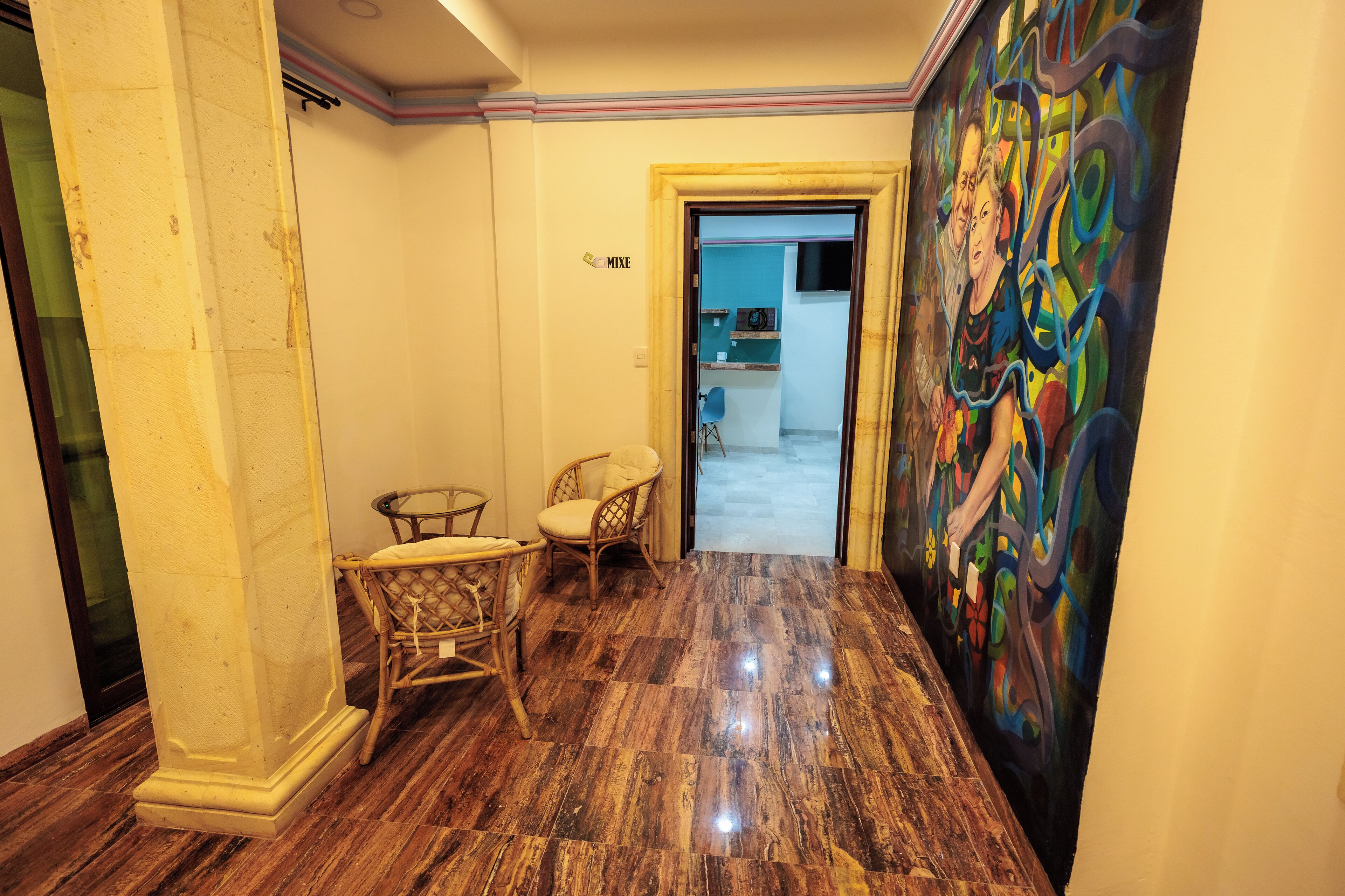 A hallway with a marble floor, a painting on the wall, and two wicker chairs.