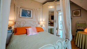 A bedroom with a four-poster bed, a nightstand, a bedside table, a chair, a table, and a mirror. - 'Courseulles Comme À La Maison' Apartment with Private Terrace and Wi-Fi (Courseulles-sur-Mer)