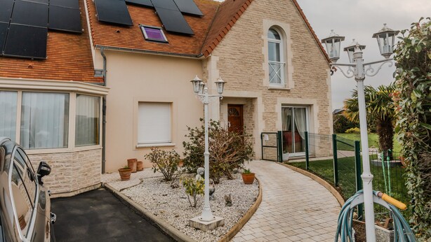 A house with solar panels, a driveway, a garden with plants, and a street lamp. - 'Courseulles Comme À La Maison' Apartment with Private Terrace and Wi-Fi (Courseulles-sur-Mer)