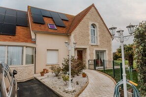A house with solar panels, a driveway, a garden with plants, and a street lamp. - Apartment 'Courseulles Comme À La Maison' with Private Terrace and Wi-Fi (Courseulles-sur-Mer)
